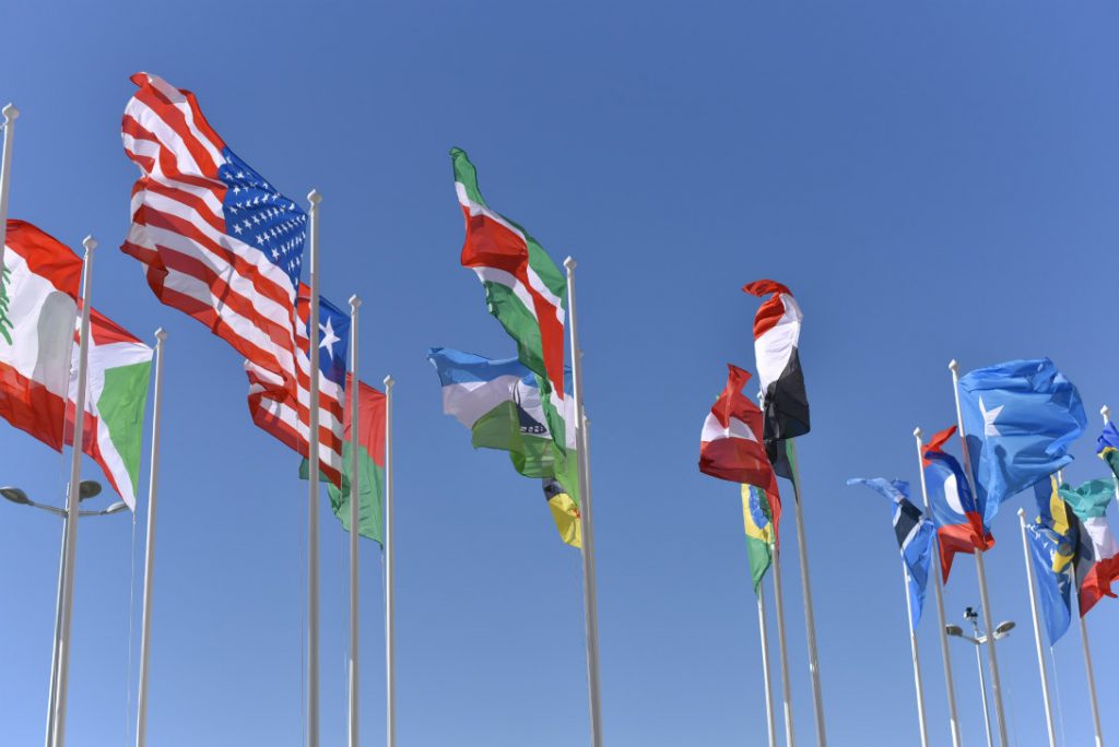 Flags from different countries blowing in the wind against a blue sky.