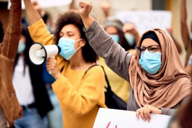 women in masks with arms raised, holding signs and a megaphone