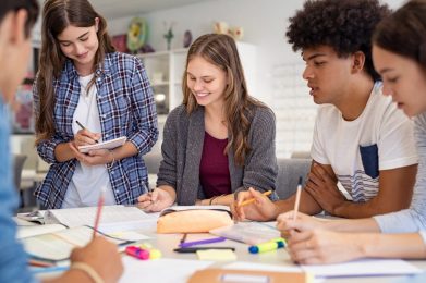 a group of youth sitting around a table, in the act of studying and smiling