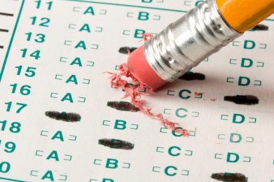a pencil, eraser-side down, being used to erase answers on a standardized testing sheet